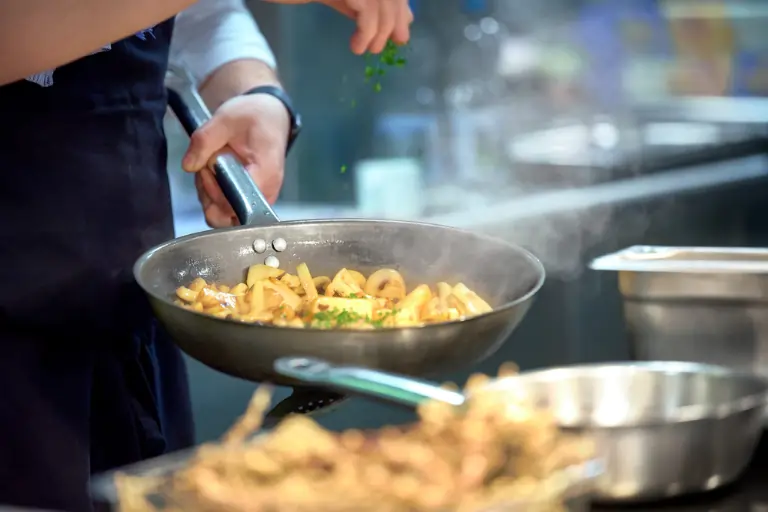 Eine Hand streut Petersilie über das Gericht in der Pfanne.