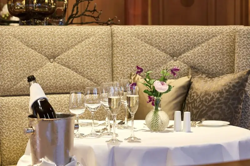 Ein gedeckter Tisch mit weißer Tischdecke und gefüllten Champagnergläser sowie einer Flasche Champagner im Kühler neben dem Tisch.