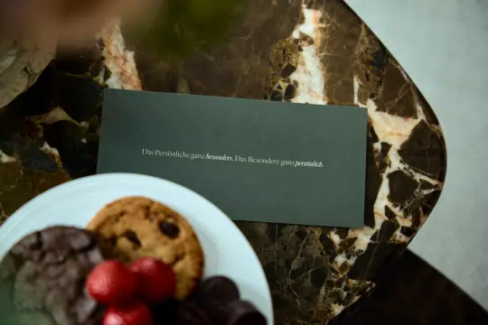 Kekse auf einem weißen Teller mit einer dunkelgrünen Begrüßungskarte auf einem Mamortisch.