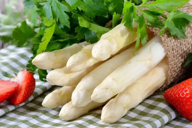 Weißer Spargel auf einem karierten Tuch und an den Seiten jeweils eine Erdbeere zur Dekoration.