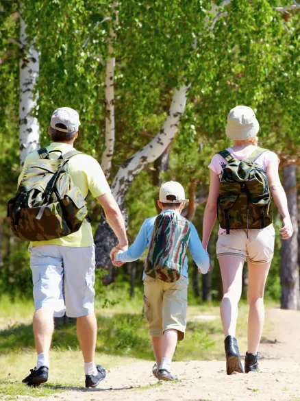 Zwischen einem Mann und einer Frau läuft ein Kind. Die Erwachsenen halten die Hand vom Kind, während sie durch den Wald laufen